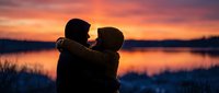 Romantic couple silhouette embracing at sunset by lake with vibrant orange and pink sky reflecting on calm water creating intimate moment for love concepts.