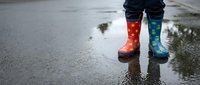 Child wearing colorful patterned rain boots standing in puddle on wet pavement after rainfall, perfect for seasonal and weather-related content.