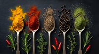 Colorful spices and herbs in wooden spoons on dark slate background. Turmeric, paprika, cumin seeds, peppercorns and green powder with fresh herbs for cooking.