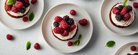 Mini chocolate cakes topped with cream, fresh raspberries and blackberries garnished with mint leaves on white plates against light background.