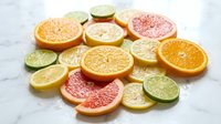 Fresh citrus fruit slices including orange, grapefruit, lemon and lime arranged on white marble surface for healthy cooking and beverage preparation.
