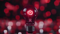 Glowing red light bulb with illuminated filament against blurred bokeh background creates dramatic atmosphere for creative and innovation concepts.