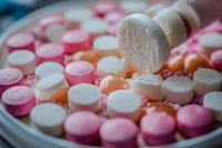 Colorful pharmaceutical pills and tablets in pink, white and orange scattered on surface, macro close-up view showing medicine texture and details.