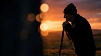Silhouette of male photographer with camera capturing sunset landscape with warm bokeh lights creating artistic outdoor photography scene.