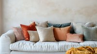 Cozy sofa with soft decorative pillows in trendy earth tones and muted colors against light wall. Minimalist home decor arrangement creates warm, inviting atmosphere.