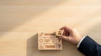 Professional businessman hand placing wooden blocks with training and development icons on desk for corporate education and skill building programs.