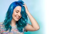 Young woman with vibrant blue hair touching her head with eyes closed, smiling peacefully against soft gradient background for beauty and wellness concepts.