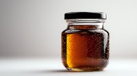 Glass jar filled with golden honey showing natural condensation droplets on surface against light neutral background, minimalist food photography composition.