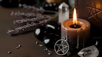Mystical altar setup with burning candle, pentagram symbols, crystals, sage bundles and ritual tools for spiritual practices and meditation ceremonies.