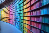 Curved modern library shelves with books arranged in rainbow spectrum colors from yellow to blue, creating striking visual pattern along curved wall. Suitable for education themes.
