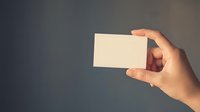 Hand holding blank white business card mockup against blurred background for branding and corporate identity design projects.