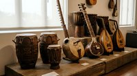 Collection of traditional African musical instruments including djembe drums, kalimba thumb pianos, and stringed instruments displayed on wooden table in warm sunlight.