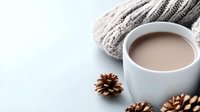 White ceramic cup filled with hot chocolate or coffee with milk against light background with knitted scarf and pine cones, cozy winter mood.