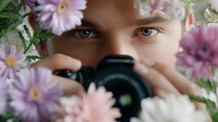 Young female photographer with camera surrounded by purple daisy flowers creating artistic portrait for creative photography and floral design projects.