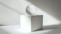Clear glass sphere on white cube pedestal casting dramatic shadows in minimalist composition against neutral background. For modern design and art concepts.