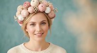 Young blonde woman wearing decorative Easter egg crown headpiece with pastel pink and beige ornaments, smiling at camera in spring portrait.