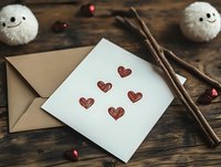 Handmade greeting card with red hearts on white paper, kraft envelope, cinnamon sticks and wool decorations on rustic wooden background for romantic occasions.