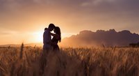 Romantic couple silhouette embracing in golden wheat field at sunset with mountain backdrop, love and intimacy concept for wedding photography.