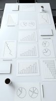 Business analytics charts and graphs spread on white desk with coffee cups for financial data analysis and strategic planning meetings.