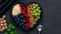 Fresh berries, nuts, oats and grapes arranged in heart shaped black plate on dark background. Healthy eating concept with superfoods and antioxidants.
