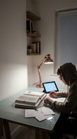 Young woman studying at home office desk with copper lamp and tablet computer during evening hours for remote learning and work productivity.
