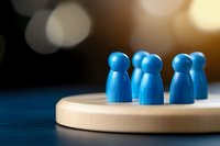 Blue wooden figures standing together on circular wooden base against blurred bokeh background, representing teamwork and community concept.