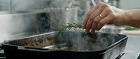 Cook adding fresh rosemary herb to steaming pot of food in kitchen, culinary preparation and seasoning ingredients for home cooking and meal preparation.