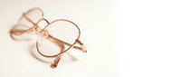 Pair of round rose gold eyeglasses with thin metal frames and clear lenses resting on neutral beige background, suitable for fashion, retail, and optical industry marketing.