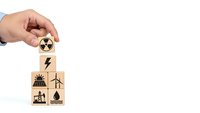Hand placing wooden cube with nuclear energy symbol on stack showing renewable power sources including solar, wind and hydroelectric on white background.