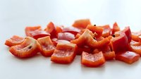Fresh red bell pepper pieces chopped and diced on white background, ready for cooking and meal preparation in kitchen.