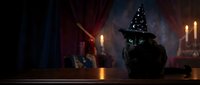 Black cat wearing witch hat sits on wooden table in candlelit room with mystical atmosphere for Halloween decorations and spooky seasonal designs.