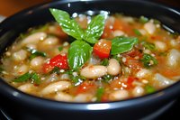 Homemade white bean soup with fresh tomatoes, herbs and vegetables in black bowl. Garnished with basil leaves, traditional Mediterranean cuisine.