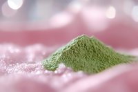 Green matcha tea powder pile on pink surface with soft bokeh lights background for wellness and healthy lifestyle concepts.