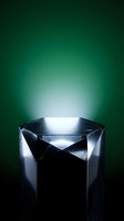 Geometric metallic pedestal with glowing green background, hexagonal dark stone podium with faceted sides for luxury product display.