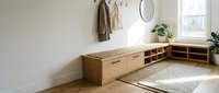 Wooden storage bench with open shelving and drawers in bright entryway with natural light, potted plants, wall hooks, and woven rug for home organization and interior design.