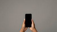 Close-up of hands holding smartphone with blank black screen against neutral gray background, suitable for app mockups and mobile technology concepts.