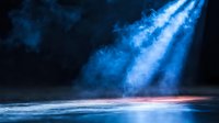 Dramatic blue light beams pierce through dark stormy clouds above calm ocean waves at twilight creating mystical atmospheric seascape for backgrounds and designs.