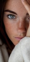 Close-up portrait of young woman with natural freckles, auburn hair and striking blue eyes wearing white sweater, showcasing natural beauty and authentic skin texture.
