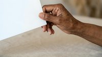 Close-up of mature adult male hand with dark skin tone touching white fabric surface, conveying texture, tactile sensation, and quality assessment for textile, material, or product evaluation.