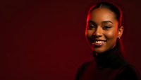 Young African American woman smiling confidently in black turtleneck against red background with dramatic lighting for professional headshot photography.