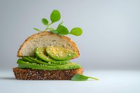 Whole grain bread sandwich with sliced avocado and fresh microgreens on white background, isolated for food styling, healthy eating and recipe design use.
