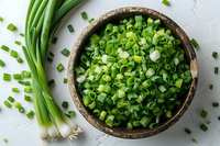 Fresh chopped green onions in rustic wooden bowl and whole scallions on white textured background, overhead view. Perfect for cooking, garnishing and food blog content.