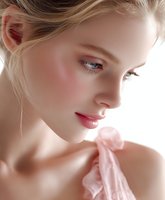 Young Caucasian woman with natural makeup and glowing skin wearing pink silk fabric, side profile portrait showing soft feminine features and delicate expression.