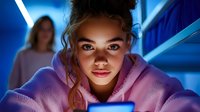 Young woman in pink hoodie illuminated by blue neon light and phone screen glow looking down at mobile device with mysterious expression, dramatic lighting creates moody atmosphere.
