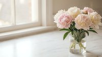 Fresh pink and white peony flowers in glass vase on white table near bright window creating elegant home decor atmosphere for interior design projects.