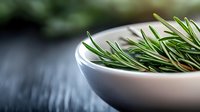 Fresh rosemary sprigs in white ceramic bowl against dark background, dramatic lighting highlights aromatic herb detail, selective focus creates depth for culinary use.