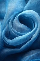 Soft blue textile fabric with delicate folds creating a rose-like swirl pattern, showcasing lightweight gauze texture for fashion or interior design.