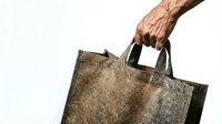 Male hand holding brown leather textured reusable shopping bag on white background for eco-friendly retail and sustainable lifestyle concepts.