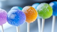 Colorful cake pops with sugar sprinkles in vibrant rainbow colors on white sticks against blurred background. Sweet dessert treats with sparkly crystal coating.