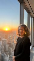 Mature Asian businesswoman enjoying sunset view from high-rise office window overlooking urban cityscape during golden hour for corporate success concepts.